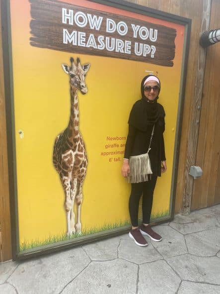 Woman measuring her height against a giraffe sign.