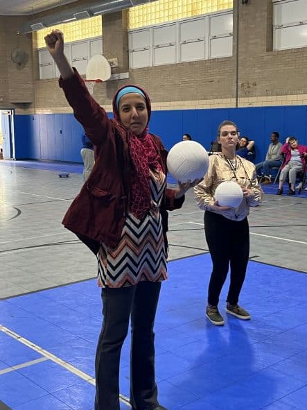 Woman holding a volleyball raising her hand.