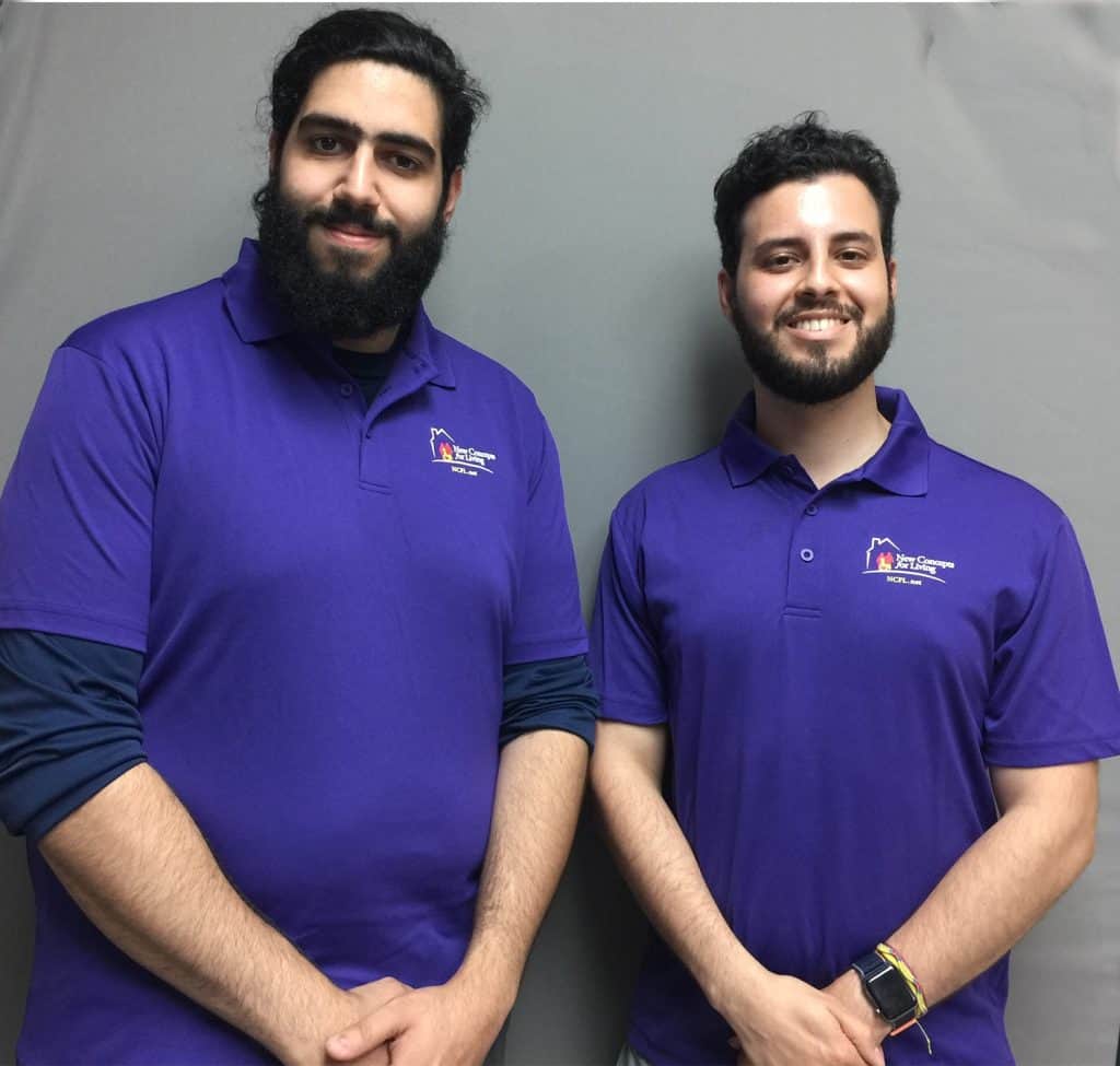 Picture of two smiling men with beards in purple New Concepts For Living shirts.