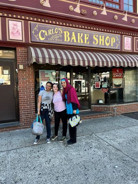 Three ladies posing for a picture in front of Carlo's Bake Shop.