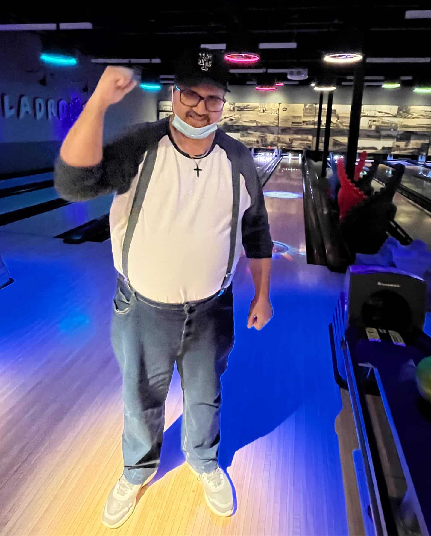 An intellectually disabled man standing in a bowling alley holding his right fist up.