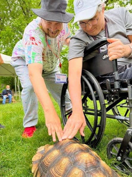 Two intellectually and developmentally disabled men in a park petting a snapping turtle.
