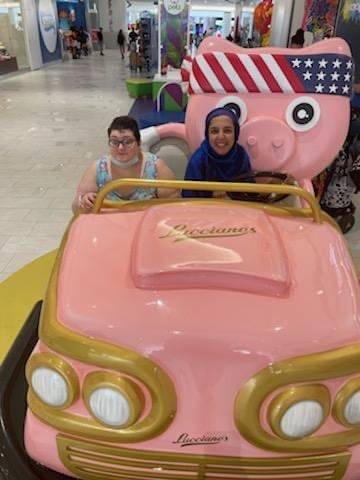 Two ladies sitting in a pink car.