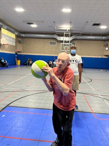 An intellectually and developmentally disabled older man holding a green and white basketball getting ready to make a throw.