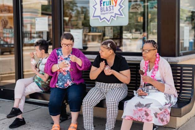 Four women sitting on a bench eating ice cream.