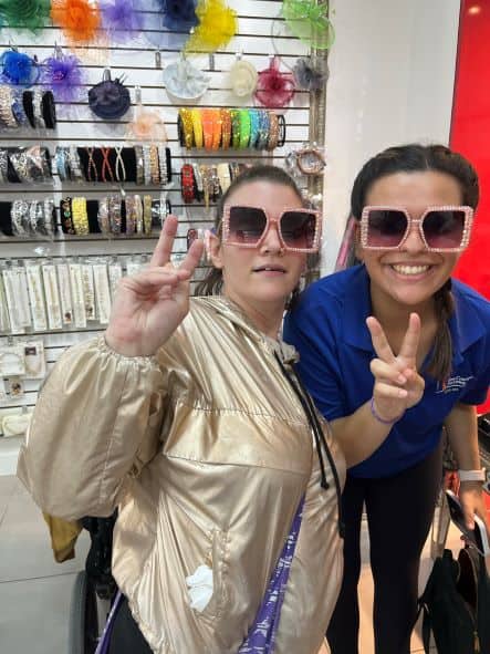 Two women wearing pink sunglasses holding up peace signs.