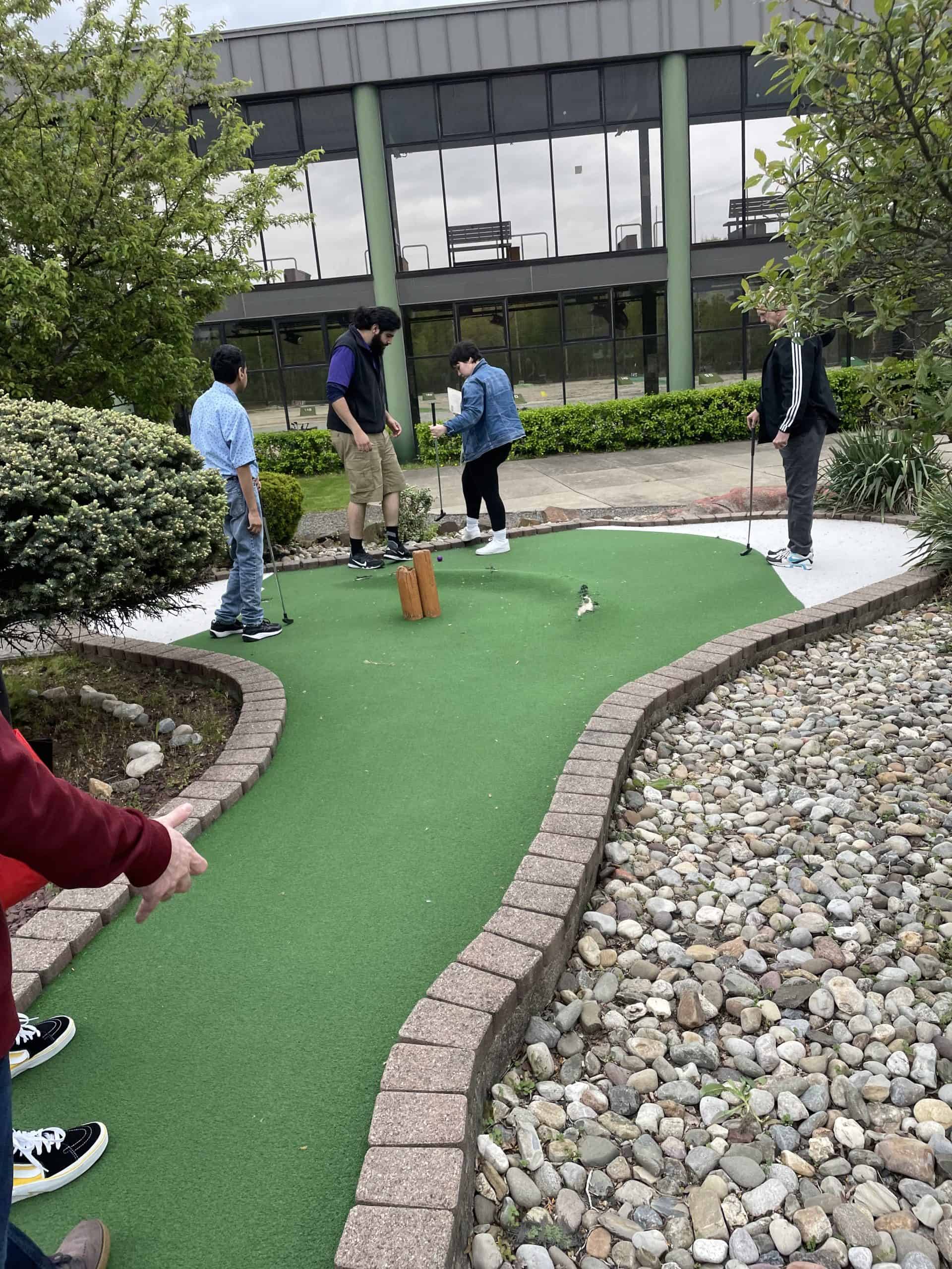 Four people standing on a mini-golf course.